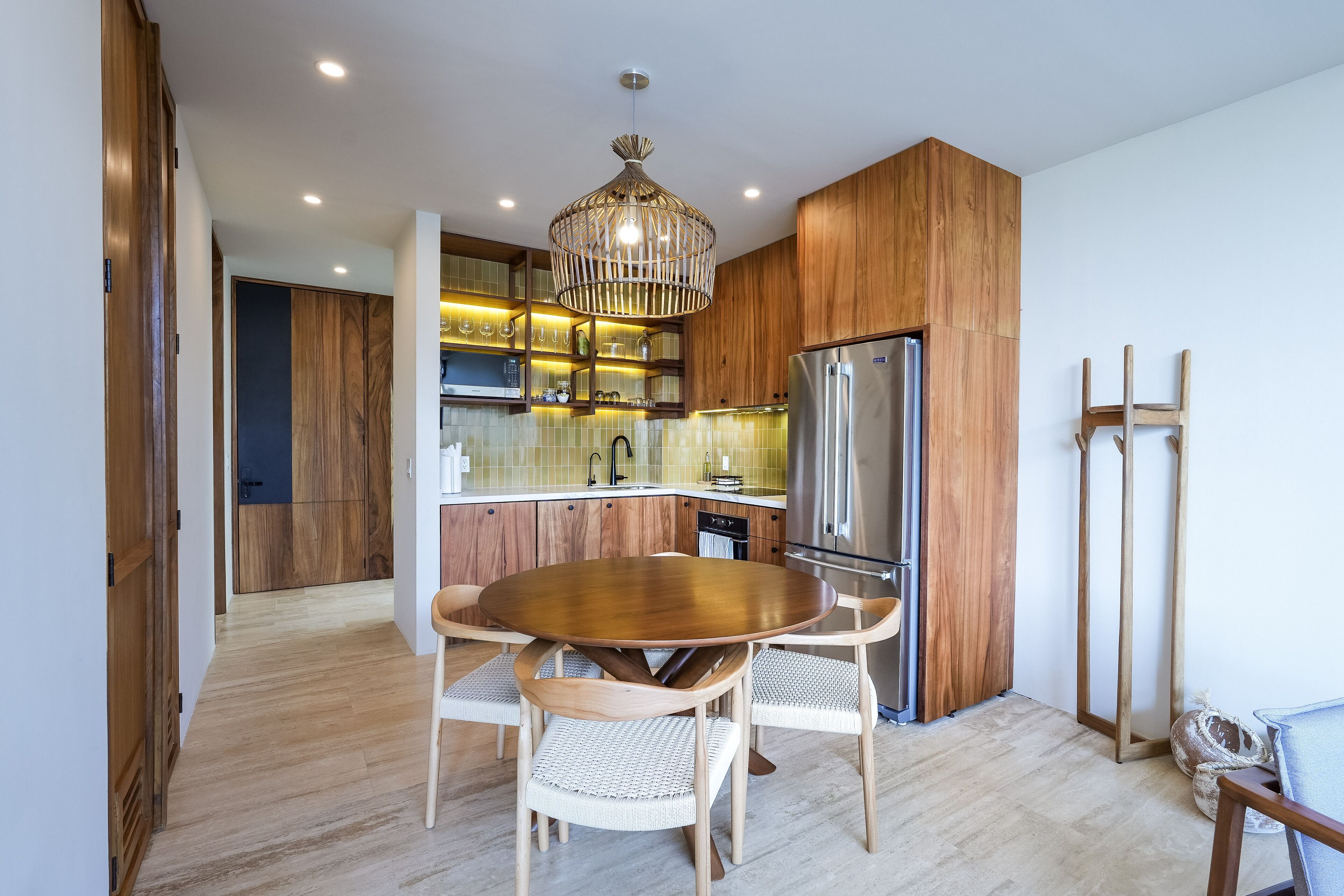 A modern kitchen with wooden cabinets, a stainless steel refrigerator, and a dining table with chairs.