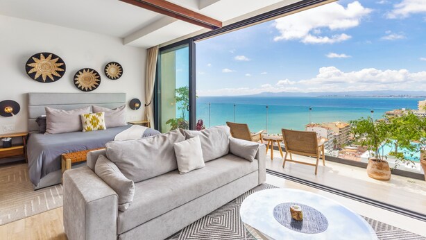 Um quarto moderno com uma grande janela, um sofá, uma cama e vista para o oceano.