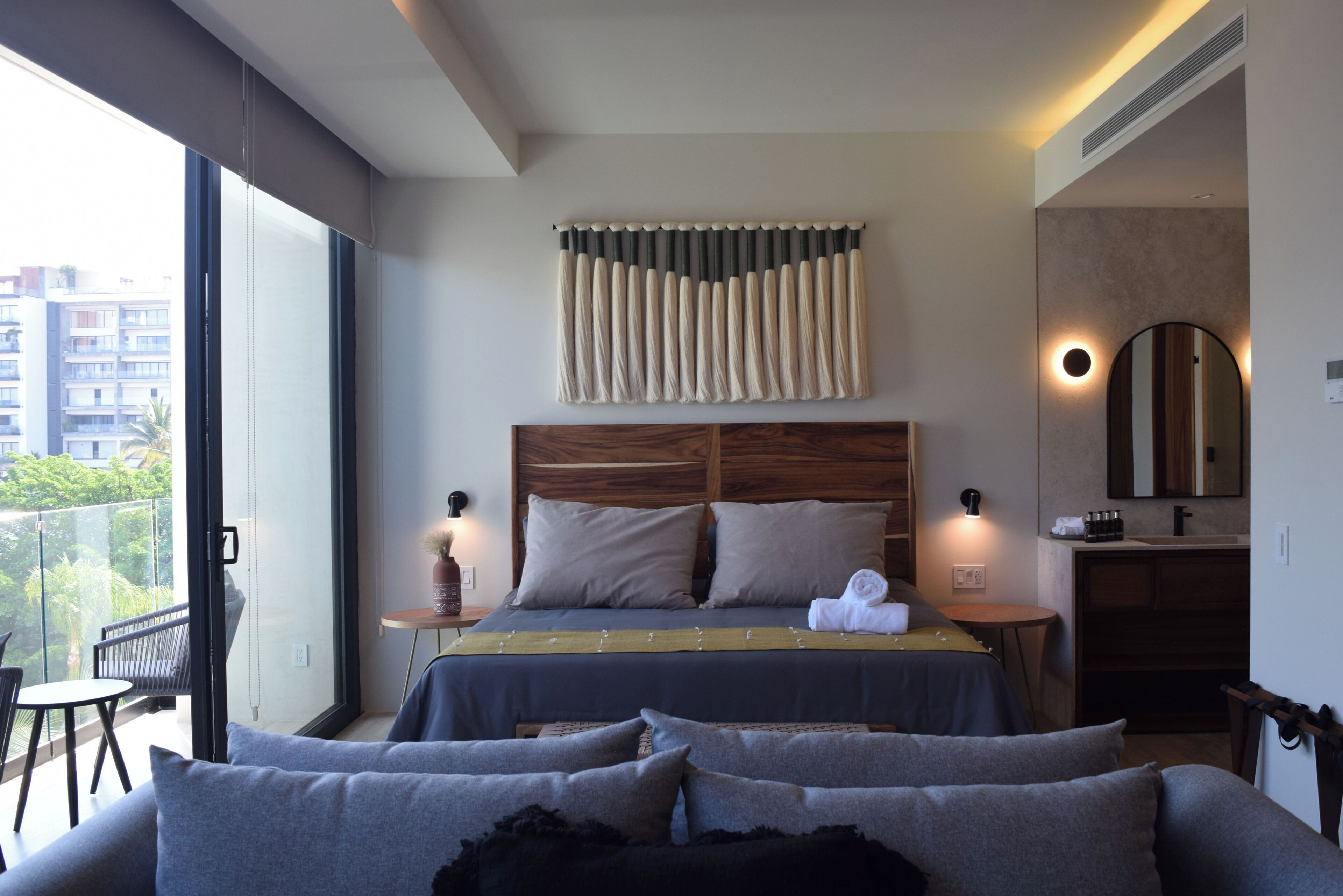 A modern hotel room with a large bed, a balcony, a round mirror, and a small table.