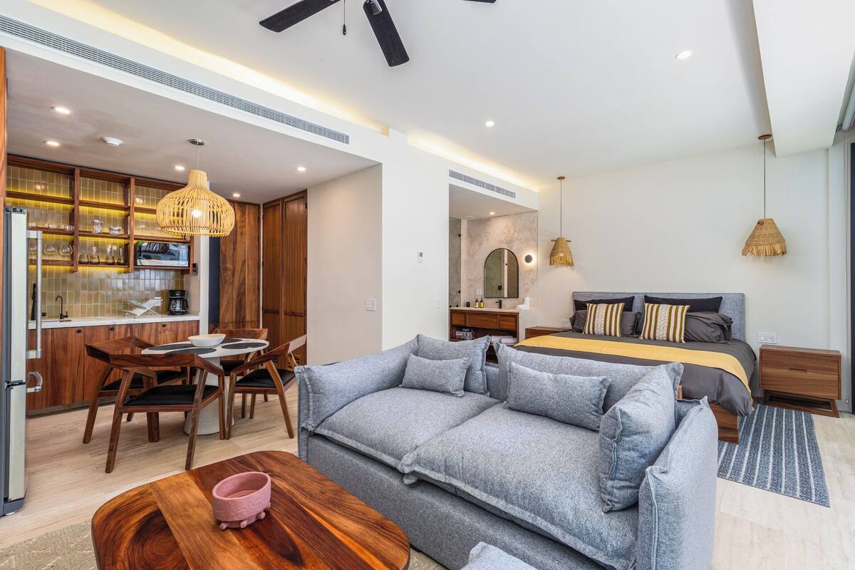 A modern living room with a sofa, dining area, and a bed with a headboard.