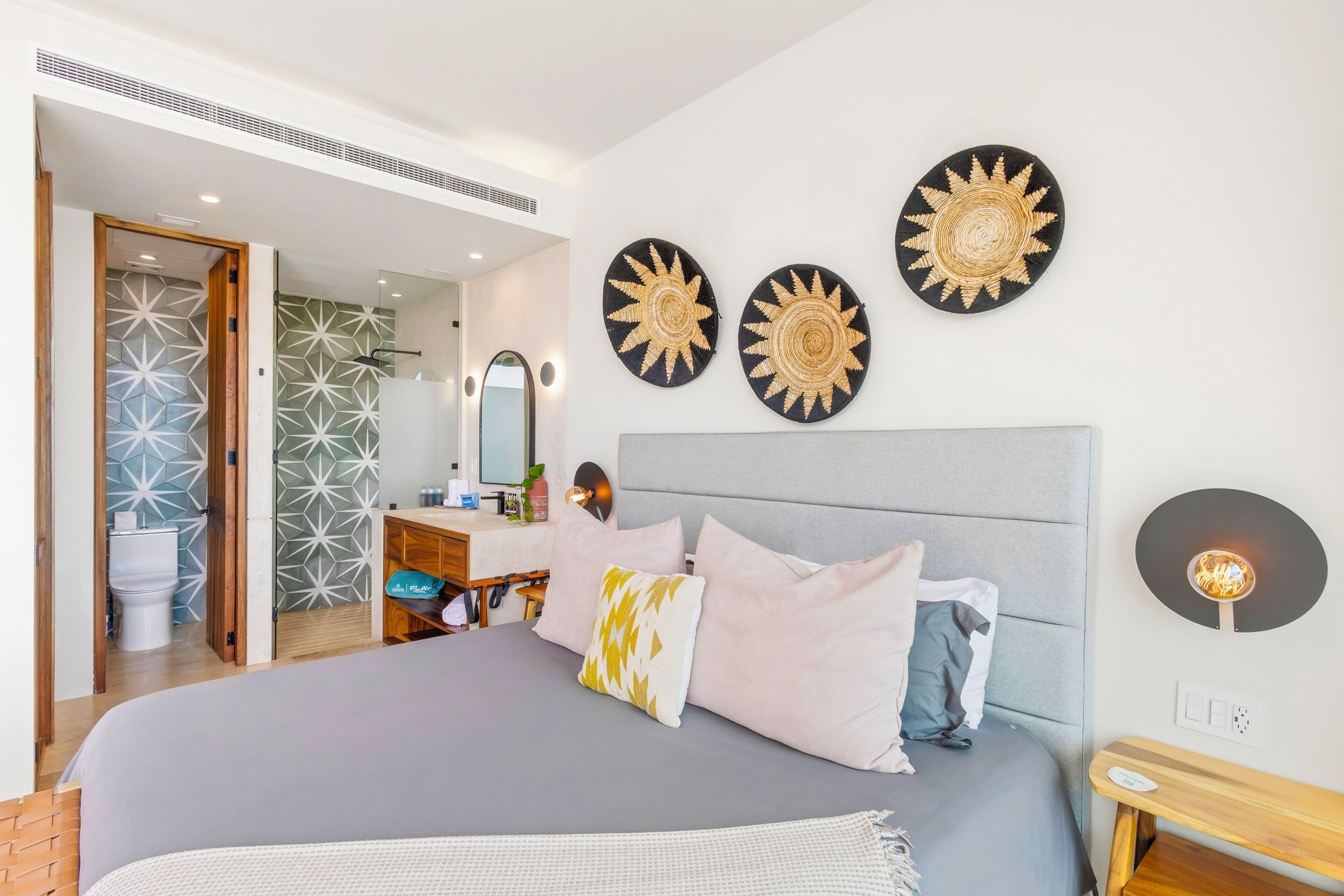 Une chambre d’hôtel moderne avec un grand lit, une table de chevet, un miroir et des œuvres d’art décoratives au mur.