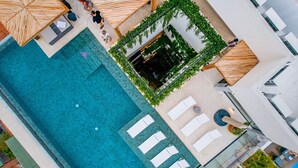 Vista aérea de uma área de piscina de hotel, com um elemento central de água, várias espreguiçadeiras e um jardim ao redor.