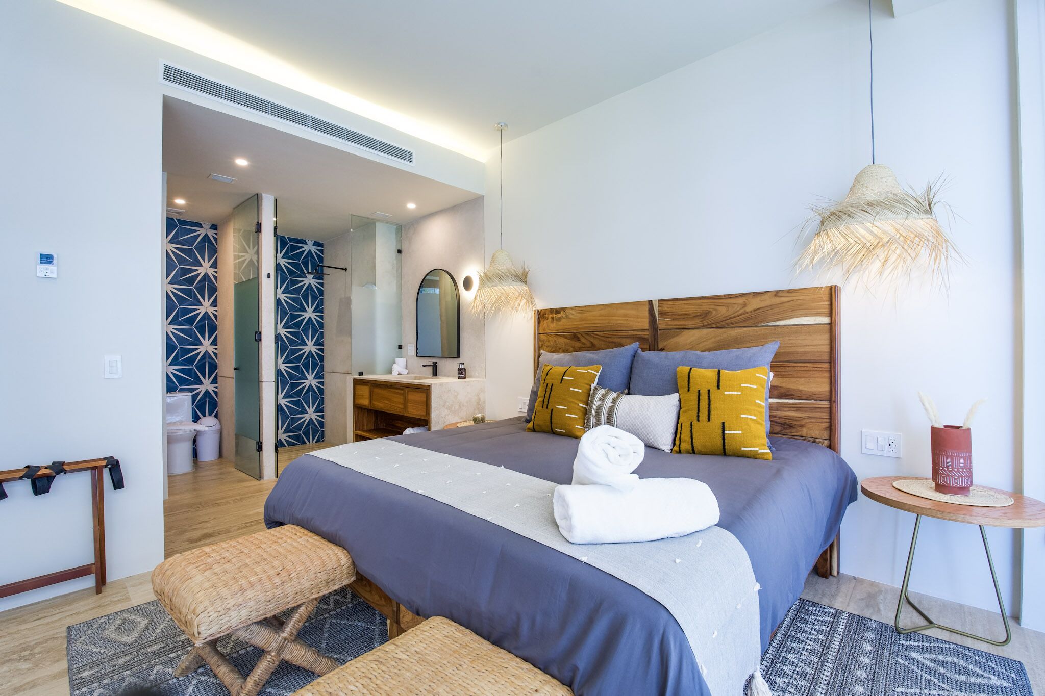 Een moderne hotelkamer met een groot bed, een houten hoofdbord en een klein rond tafeltje met een lamp.