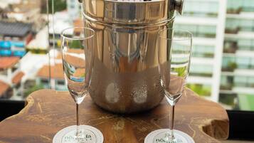Une bouteille de champagne dans un seau en métal, posée sur une table en bois, avec deux verres à proximité, et une vue sur la ville en arrière-plan.