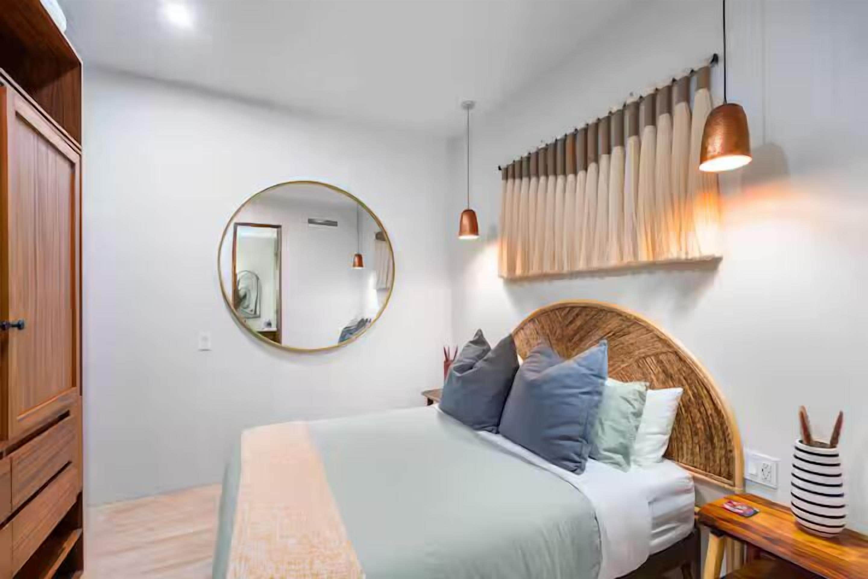 Une chambre à coucher avec un lit, un miroir rond, une armoire en bois et un luminaire suspendu.