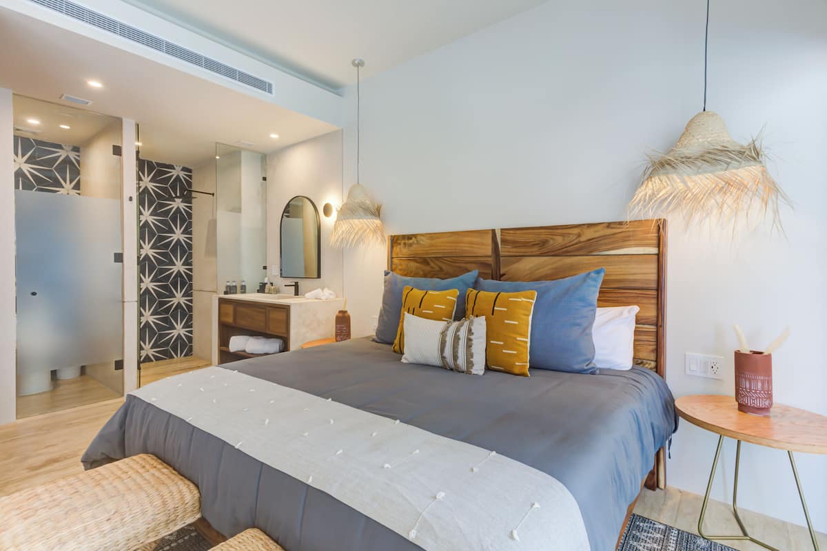 A modern bedroom with a large bed, bedside tables, a mirror, and a small round table with a vase.