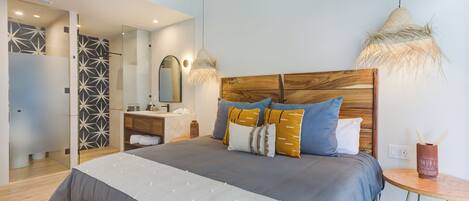 Un dormitorio moderno con una cama grande, mesitas de noche, un espejo y una pequeña mesa redonda con un florero.