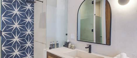 A modern bathroom with a geometric tile backsplash, a large mirror, and a white sink with wooden cabinets.