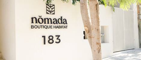 Een bordje voor 'Nomada Boutique Habitat' op nummer 183, met een minimalistisch ontwerp, een logo en de naam van de accommodatie.