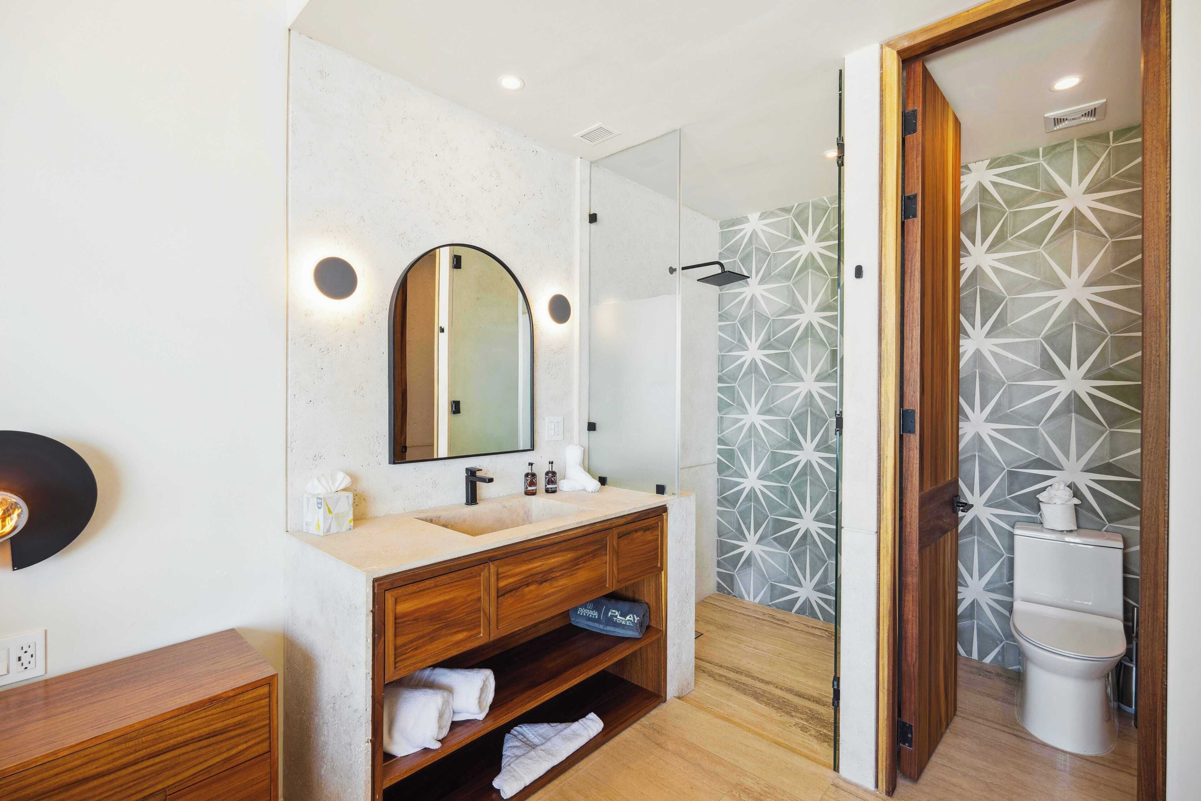 Un baño moderno con tocador de madera, un espejo grande, ducha con azulejos de diseño geométrico y un inodoro.