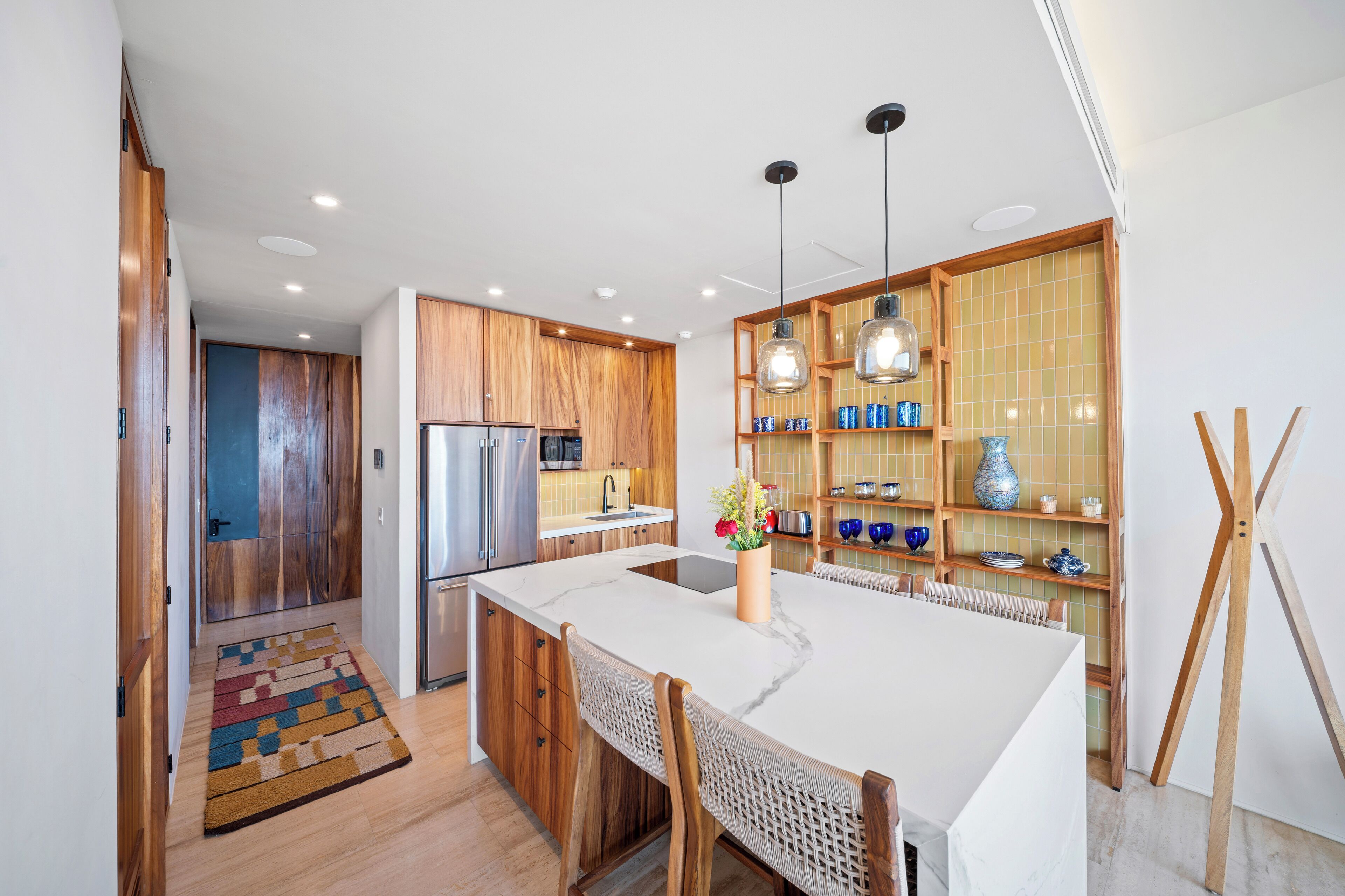 Una cocina moderna con armarios de madera, una isla central, iluminación colgante y un salpicadero de azulejos.
