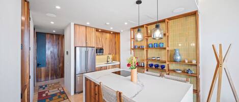 Una cocina moderna con armarios de madera, una isla central, iluminación colgante y un salpicadero de azulejos.