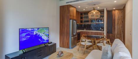 Een moderne woonkamer met een flatscreen televisie, houten meubels en een keukenhoek met houten kastjes en een inbouwoven.