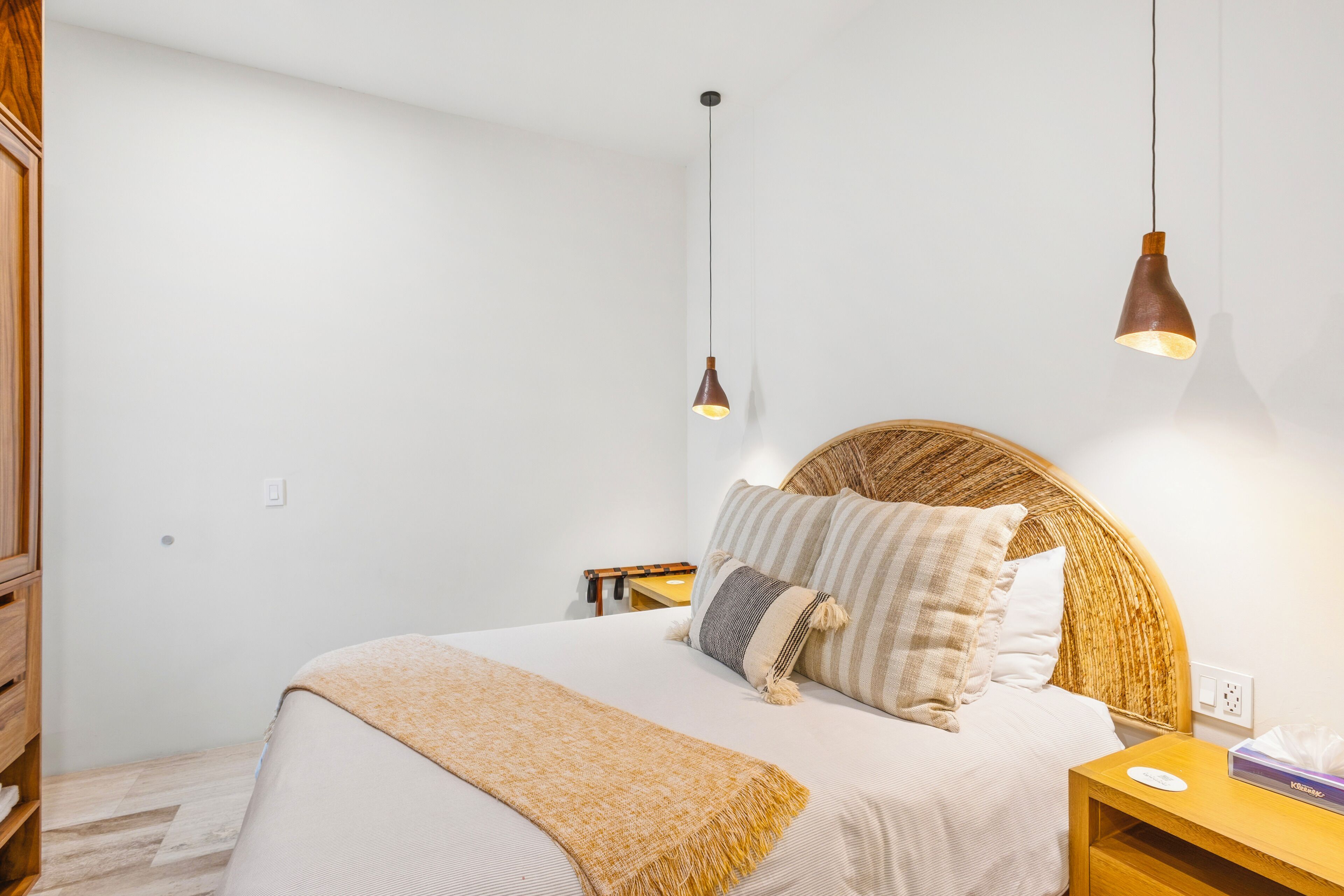 Un dormitorio con cama, mesitas de noche, cabecera de madera y lámparas colgantes.