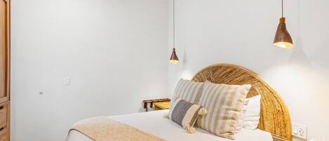 A bedroom with a bed, bedside tables, a wooden headboard, and pendant lights.