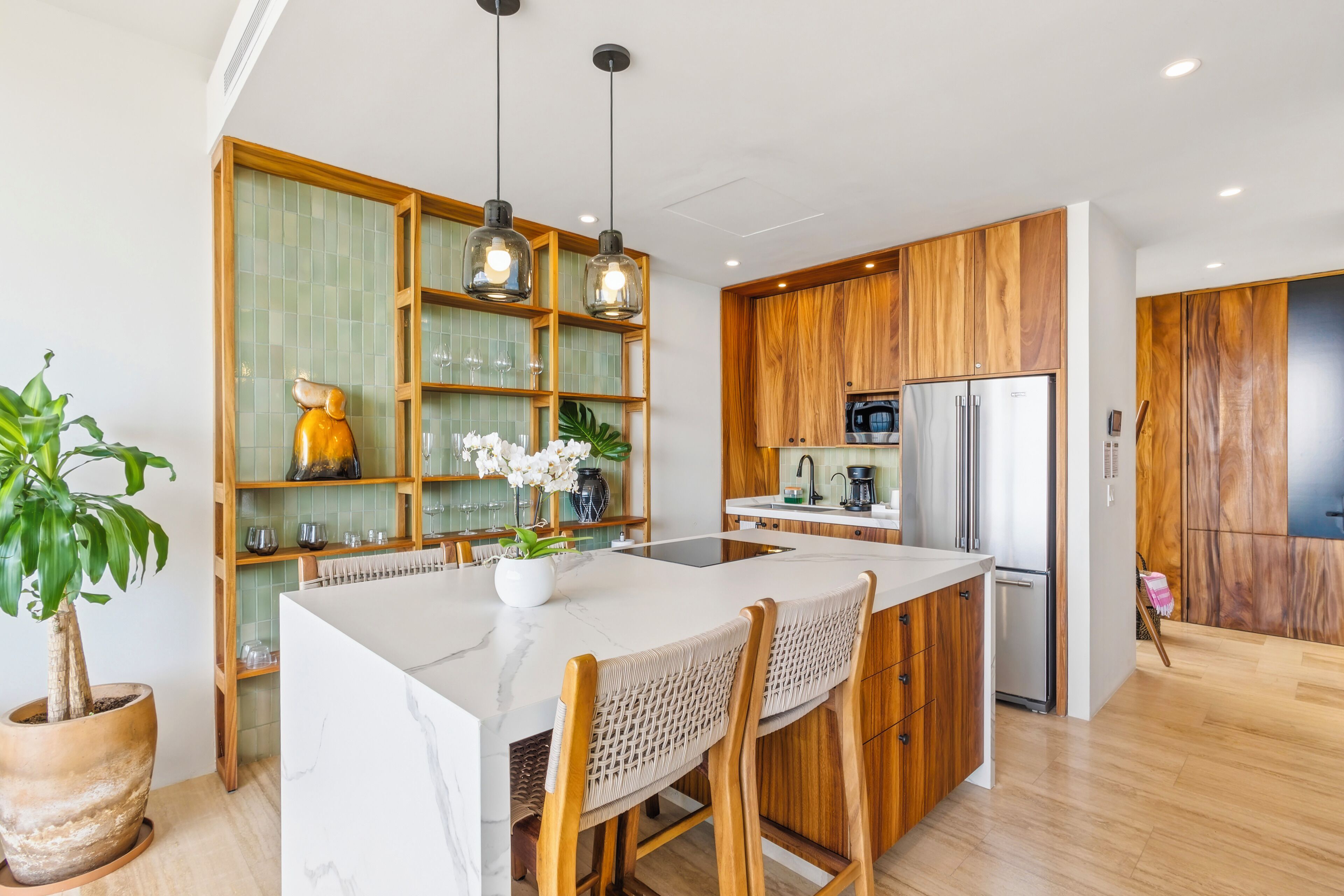 Een moderne keuken met houten kastjes, een marmeren aanrechtblad en hanglampen.