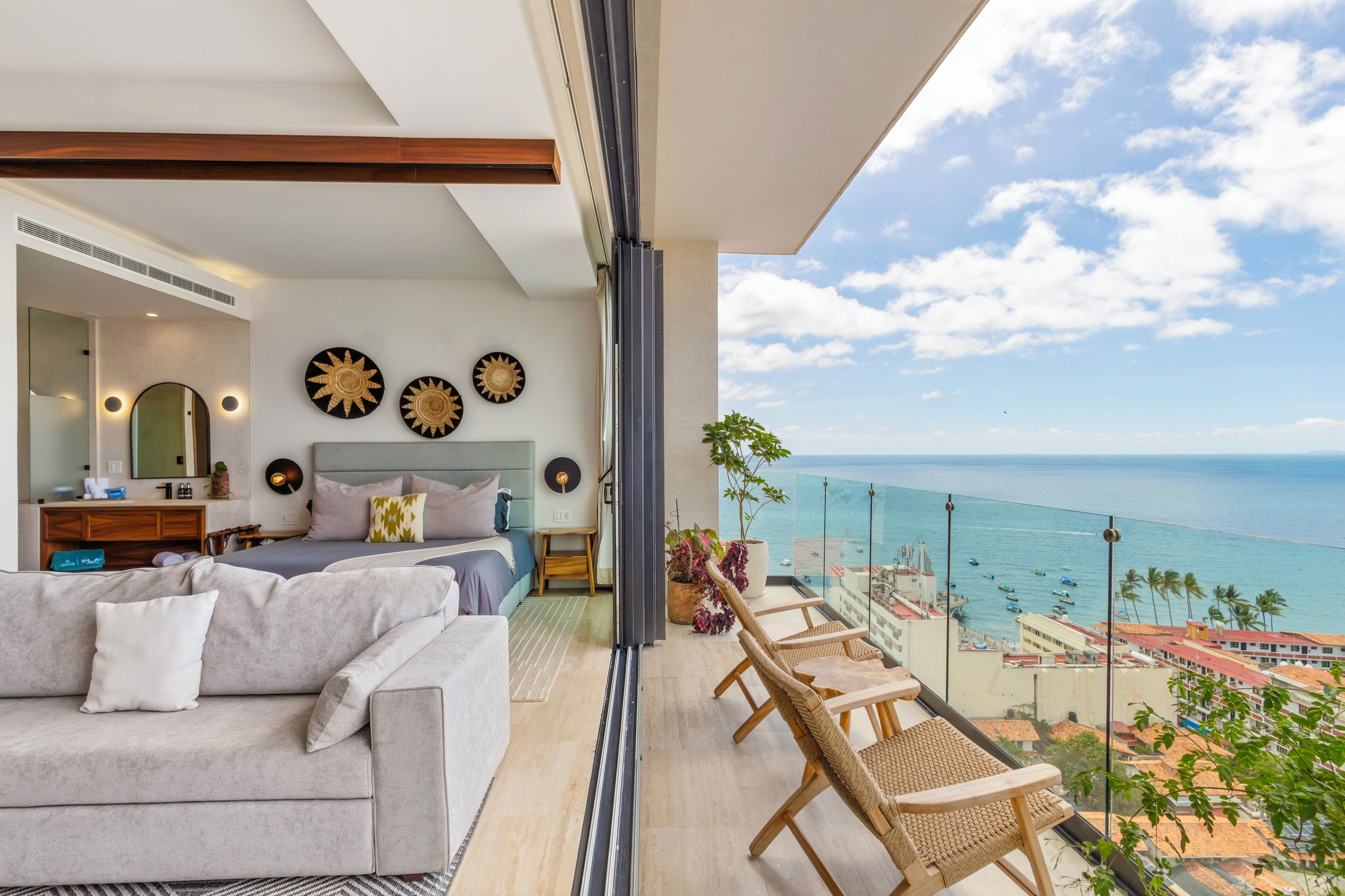 A balcony with a view of the sea, a bedroom with a bed and a dresser, and a living area with a sofa and a coffee table.