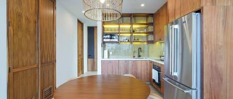 A modern kitchen with wooden cabinets, a stainless steel refrigerator, a round dining table, and a hanging light fixture.