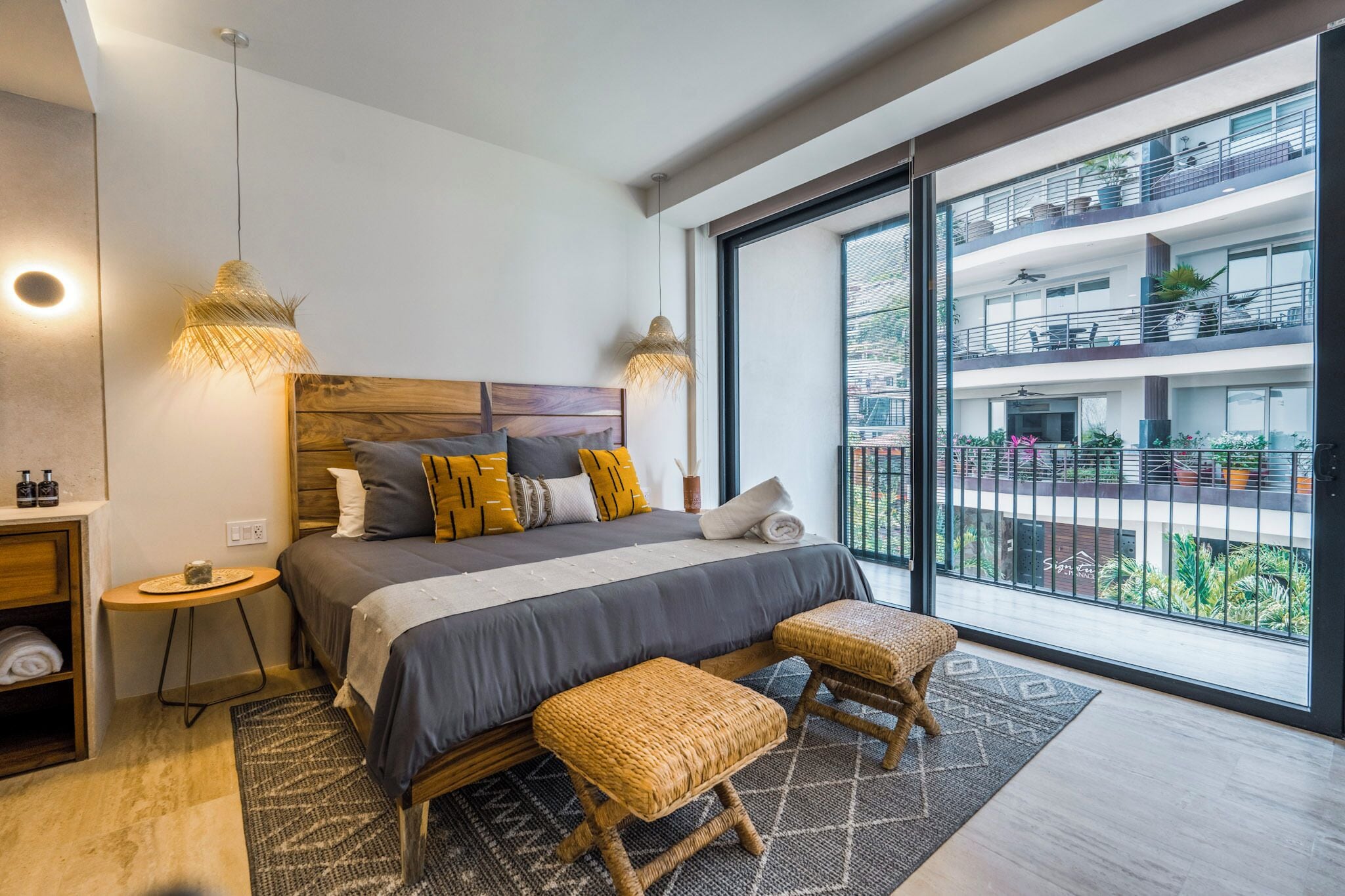 A modern bedroom with a large bed, two bedside tables, a small round table, and a large window with a balcony view.