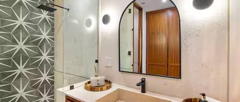 A modern bathroom with a geometric-patterned wall, a large mirror, a sink, and wooden cabinetry.