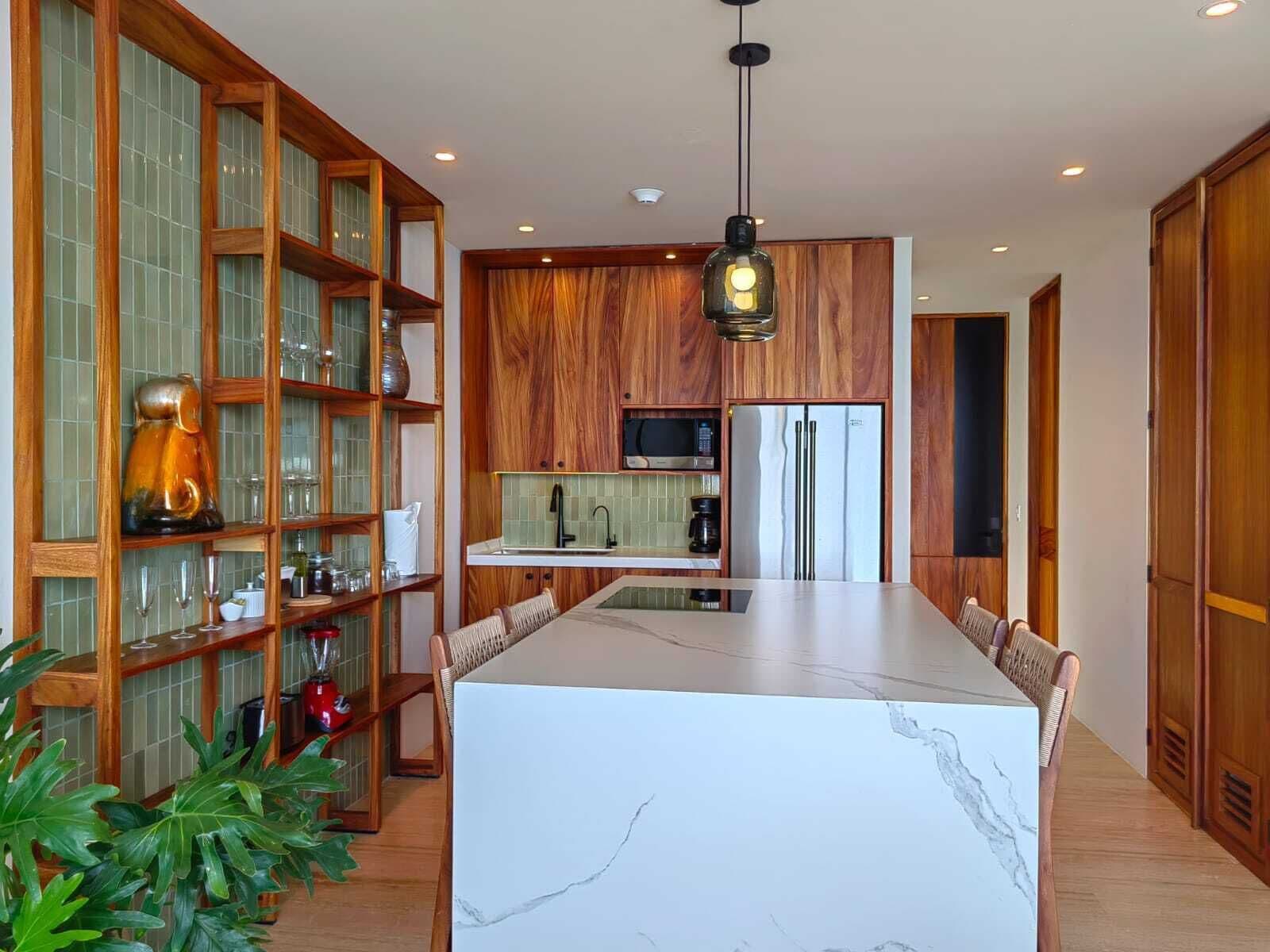 A modern kitchen with wooden cabinets, a marble island, and a hanging light fixture.