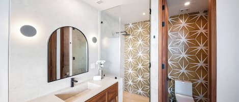 Un baño moderno con un espejo grande, un lavamanos y una zona de ducha.
