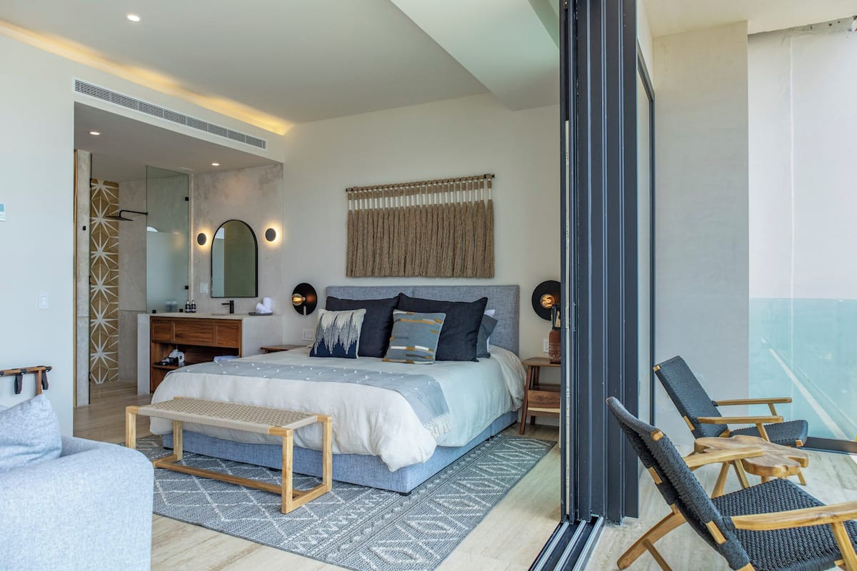 A modern bedroom with a large bed, bedside tables, a bench, and a view of the outside.
