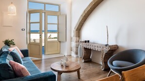 Un salon avec un canapé, une table ronde en bois et une chaise. Une grande fenêtre offre une vue sur la plage.