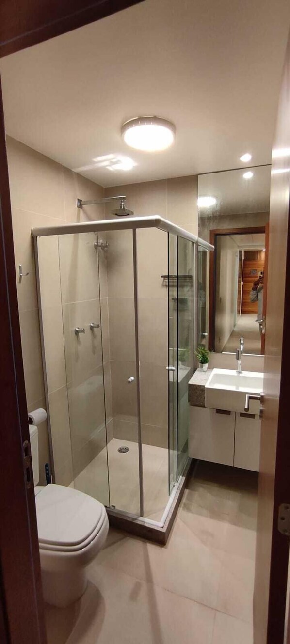 A modern bathroom with a glass-enclosed shower, a toilet, and a sink with a mirror above it. - RESERVA DOS CARNEIROS BEIRA MAR (Tamandaré)