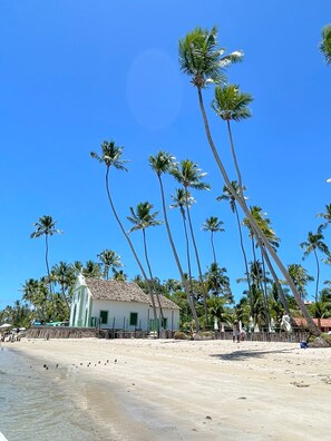 A beach with tall palm trees and a small building with a tiled roof. - RESERVA DOS CARNEIROS BEIRA MAR (Tamandaré)