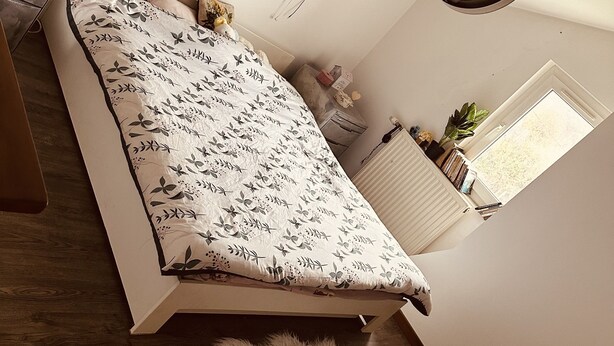 Un dormitorio con una cama, una guitarra, una ventana, una planta y una lámpara de pared.