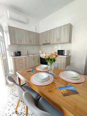 A modern kitchen with wooden cabinets, a microwave, and a coffee maker. There is a dining table with plates and a vase of flowers.