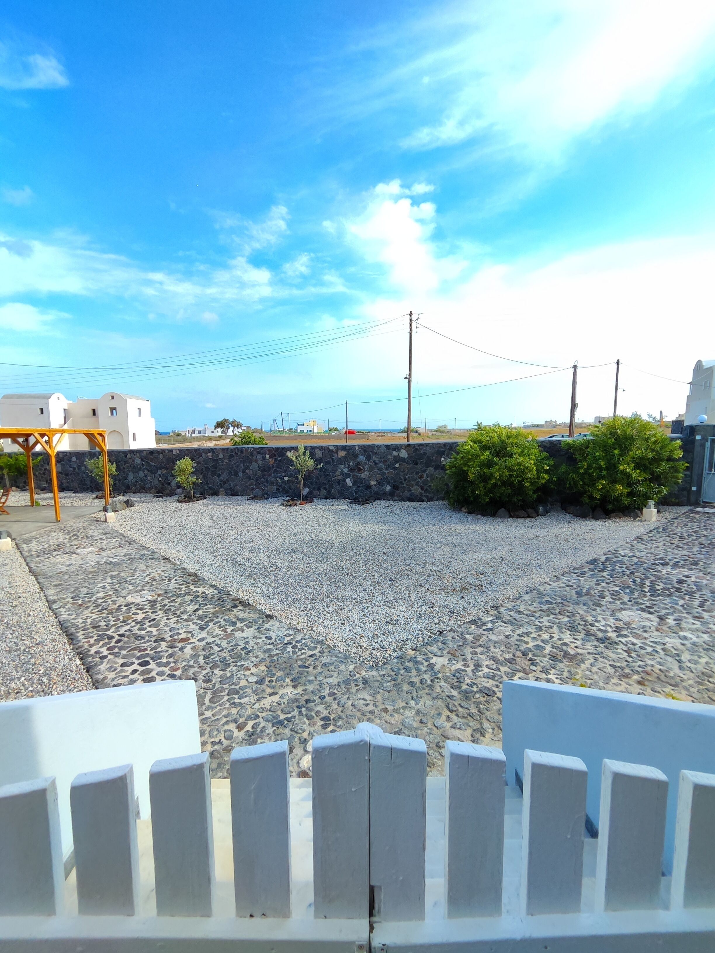 A courtyard with a gravel path, a stone wall, and a view of buildings in the distance.
