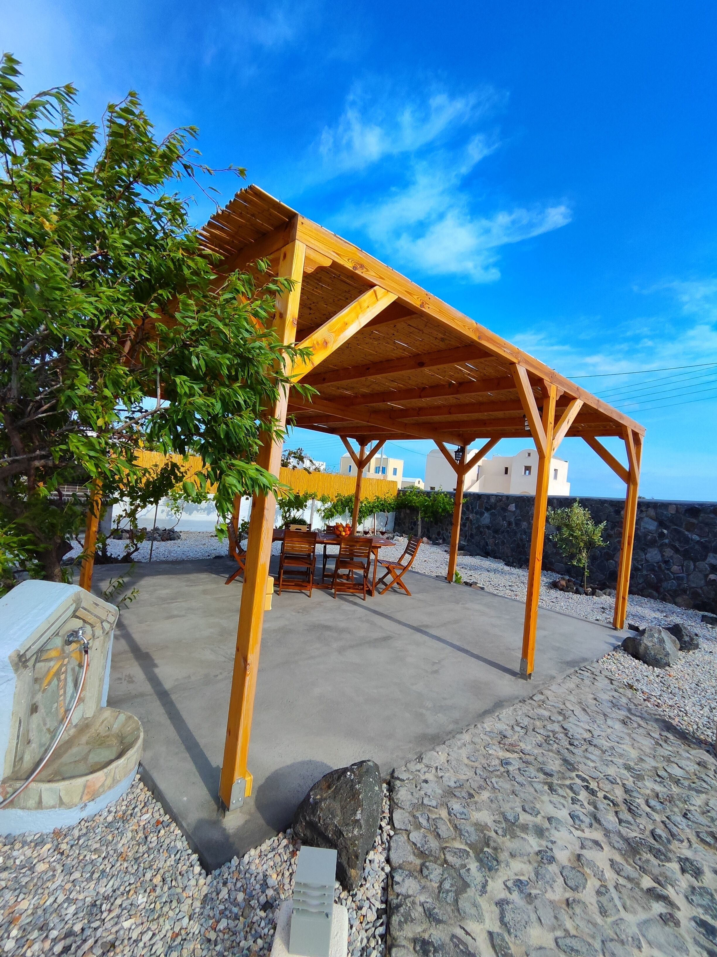 Une pergola en bois, avec une table et des chaises, entourée de gravier et de petits rochers.