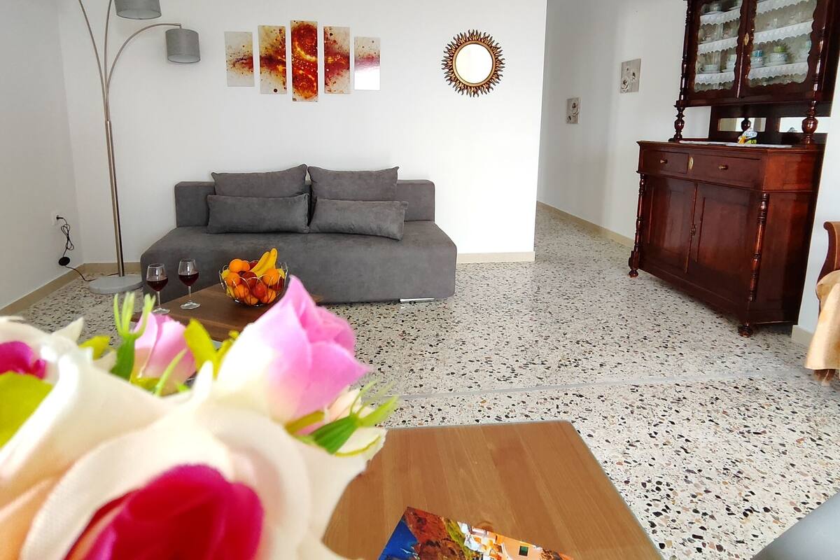 A living room with a grey sofa, a wooden cabinet, and a coffee table with a book and flowers.