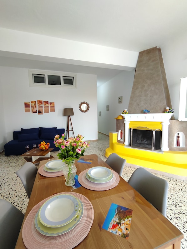 A dining area with a wooden table set for four, a vase with flowers, and a fireplace with colorful decorations.