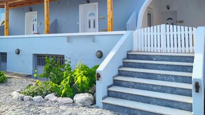 A white building with a wooden pergola, stone steps, and a garden area. - Oasis Apartments (Santorini)