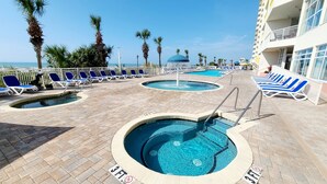 A pool area with multiple pools and lounge chairs, surrounded by palm trees and a building with balconies.