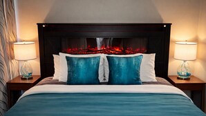 Un lit avec une tête de lit, deux lampes de chevet et une cheminée où l’on peut voir les flammes.