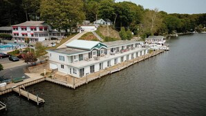 Une péniche amarrée à un quai, dotée d’une terrasse couverte, et entourée d’arbres et d’autres bâtiments, le tout situé en bord de mer.