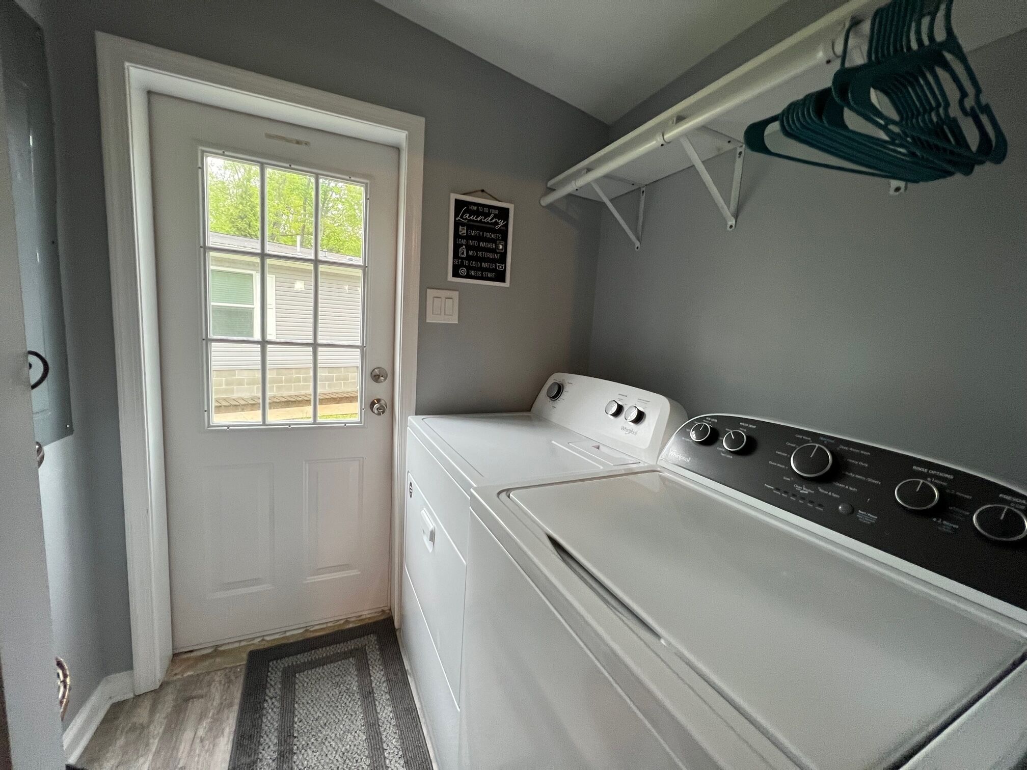 A laundry room with a white washer and dryer, a door with a window, and a wall-mounted drying rack.