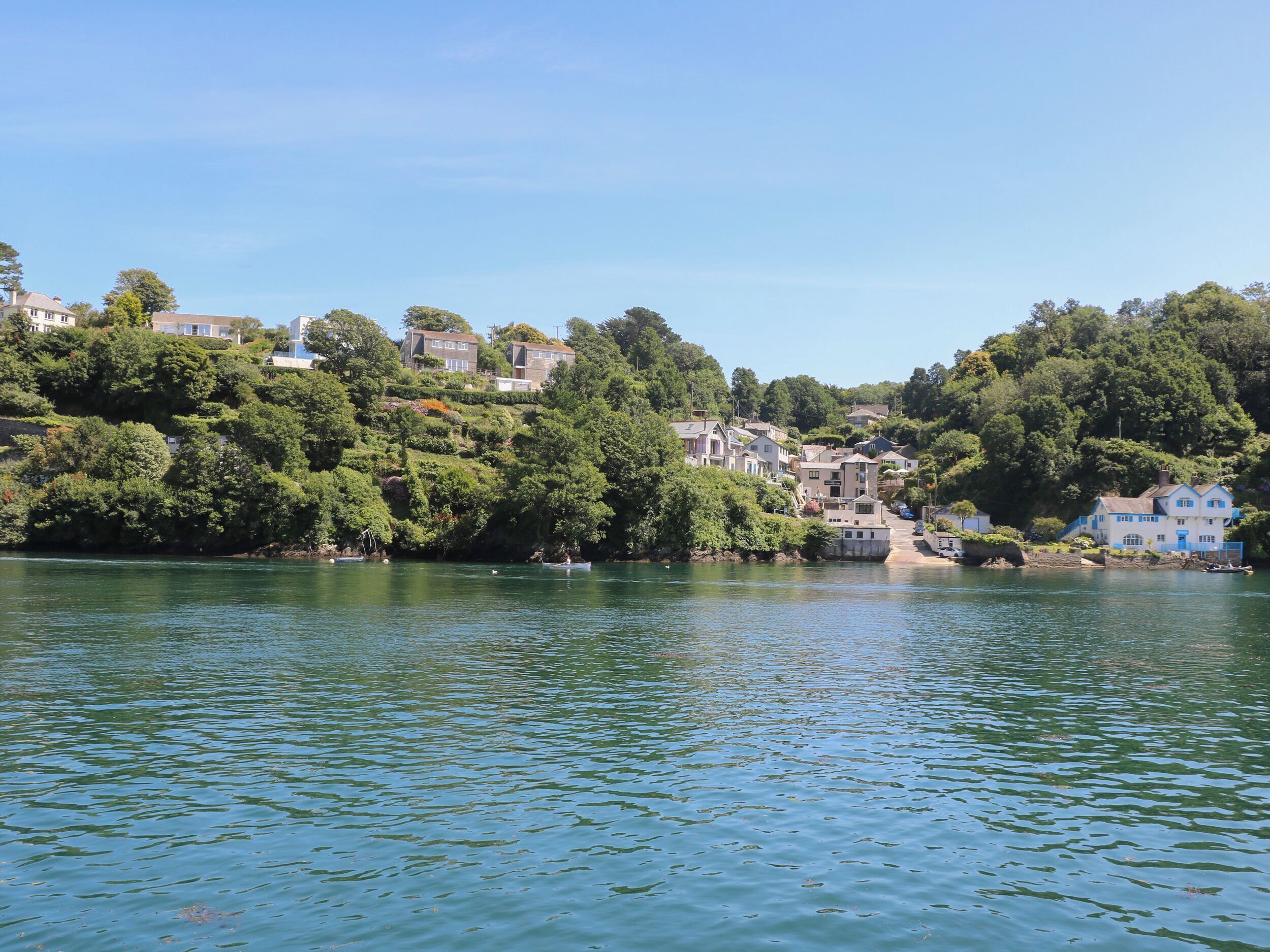 Un quartier résidentiel au bord d’un lac, avec des maisons construites sur une colline, une eau calme et un ciel dégagé.