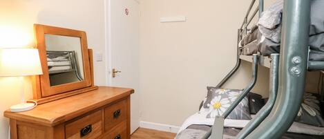 A bunk bed with a metal frame, a wooden dresser with drawers, a bedside lamp, and a door with a no entry sign.