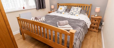 A bedroom with a wooden bed, grey bedding, two bedside tables with lamps, a window with curtains, and wall art.