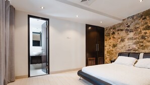 A modern bedroom with a large bed, a stone accent wall, and a bathroom visible through an open door. - Casa Azul (Panama City)