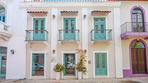 A building with three balconies, each with a green door and window, and a small entrance with a glass door. - Casa Azul (Panama City)