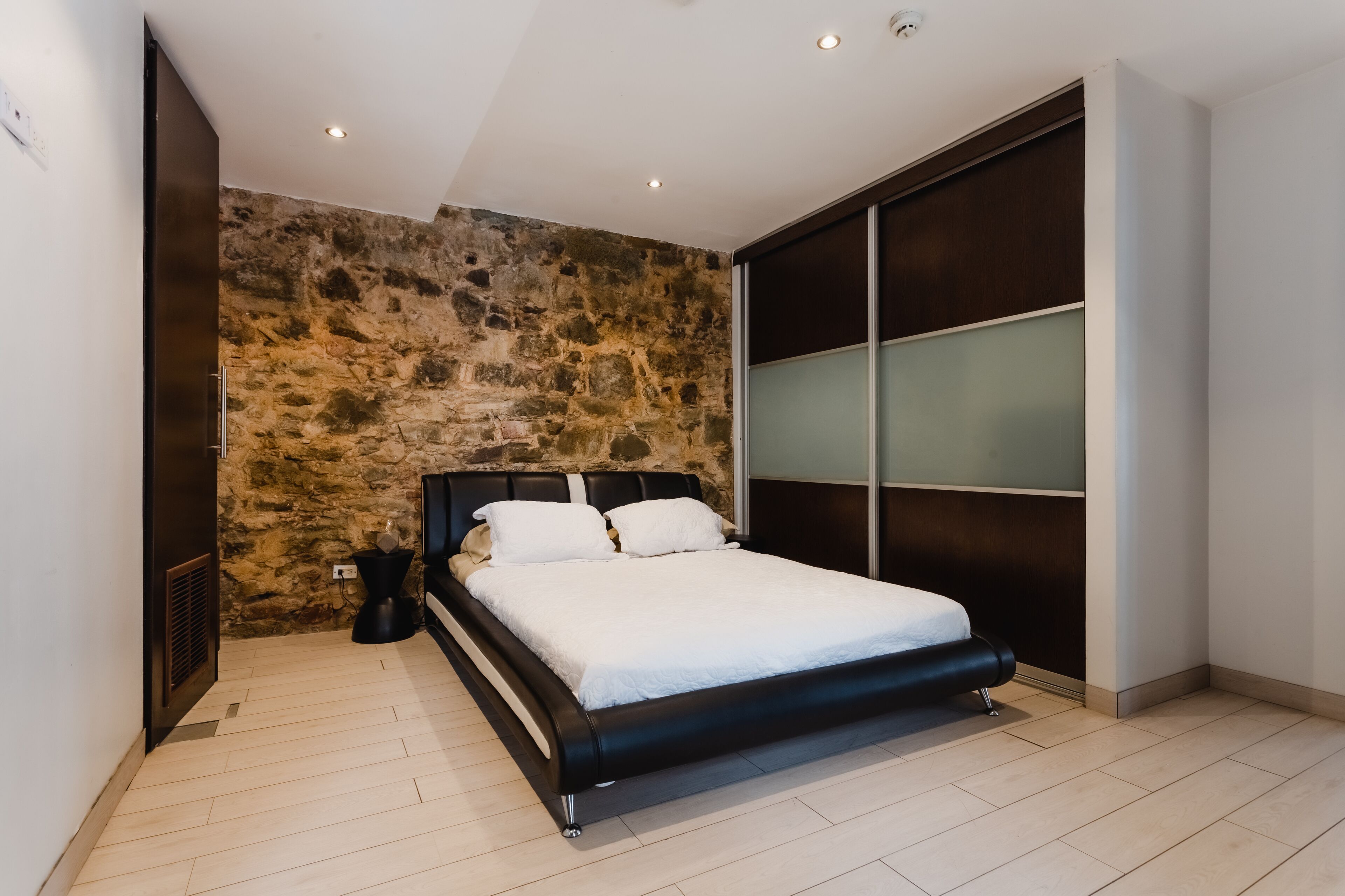 A modern bedroom with a stone accent wall, a large bed, and a sliding glass door.