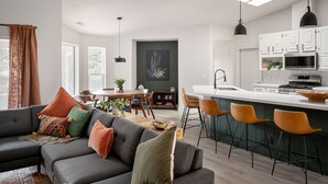 Una sala de estar moderna con un sofá gris, un comedor y una cocina con armarios blancos y salpicadero verde.