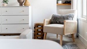 Una sala de estar moderna con un sofá blanco, una silla de mimbre, una mesita de madera y un televisor en la pared.