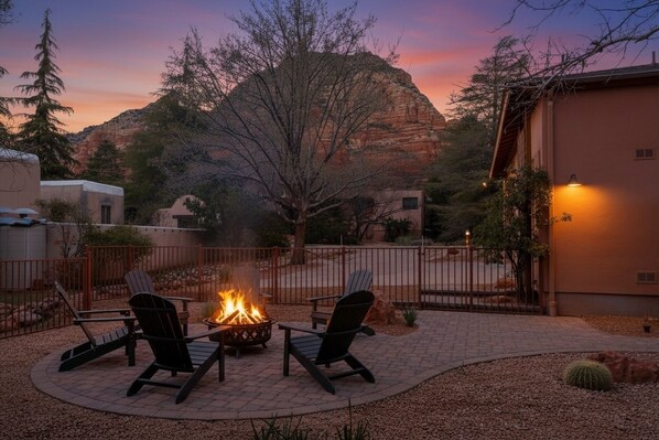 A patio with two chairs and a fire pit, surrounded by a fence and a view of a mountain.